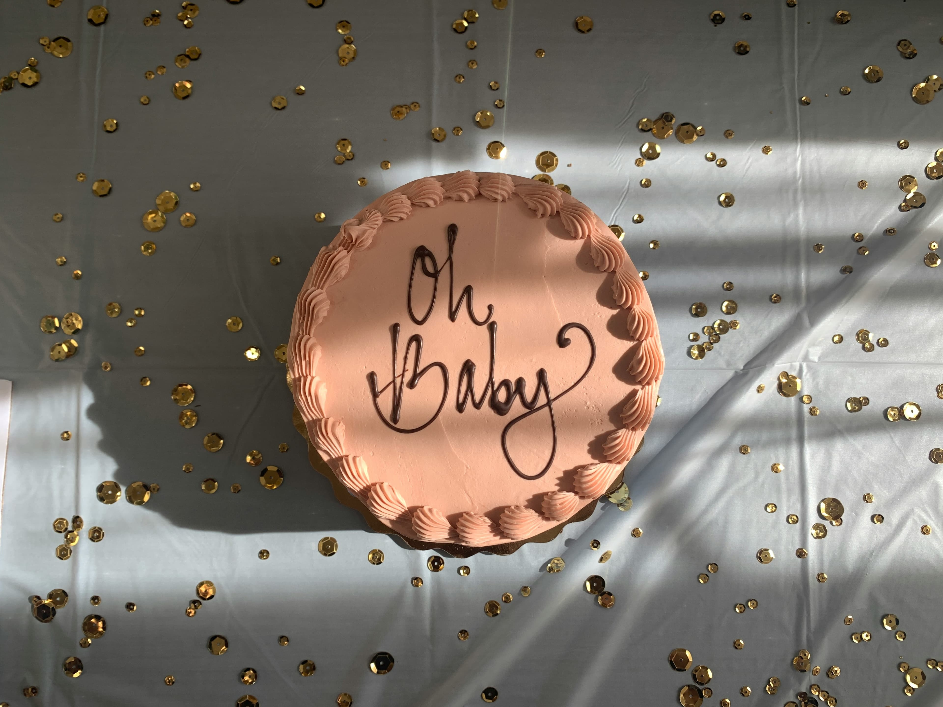 A blush “Oh Baby” cake scattered with gold confetti at a baby shower