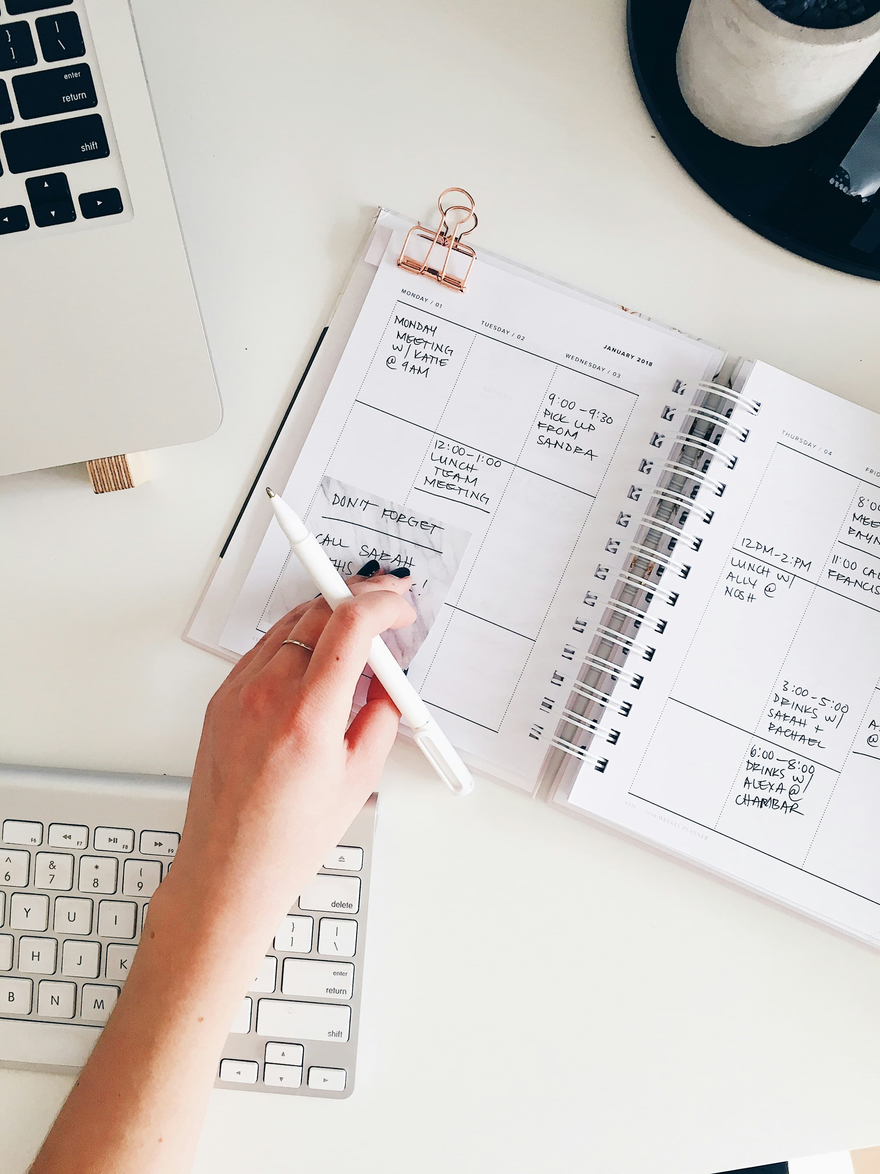 Hands mapping out an event timeline in a planner beside a laptop