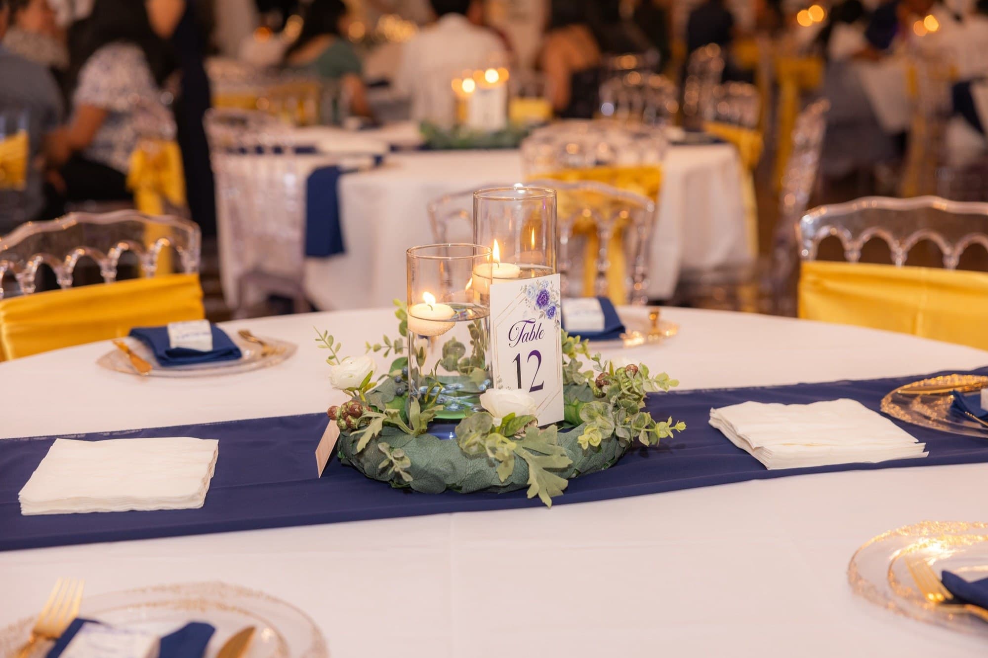 Centro de mesa con velas flotantes, follaje y número de mesa en azul