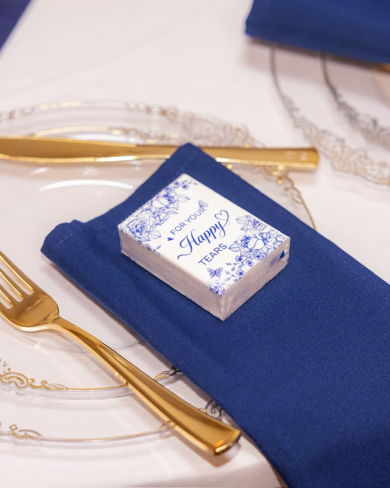 Montaje de mesa con servilleta azul, cubiertos dorados y detalle de lágrimas felices