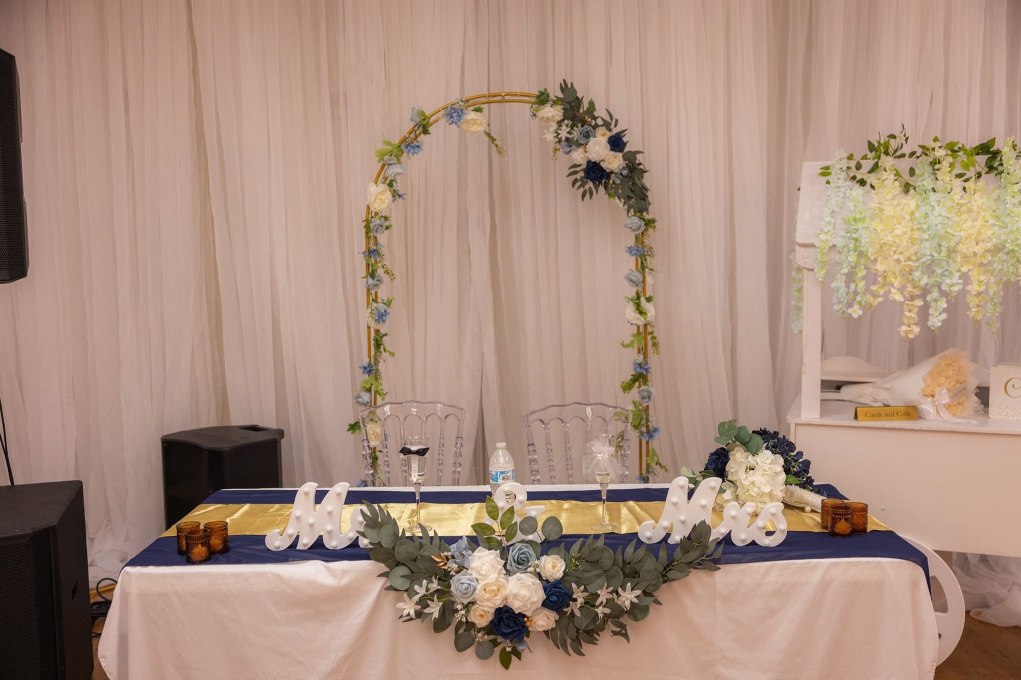 Mesa de novios con arco floral, letras Mr & Mrs y camino dorado